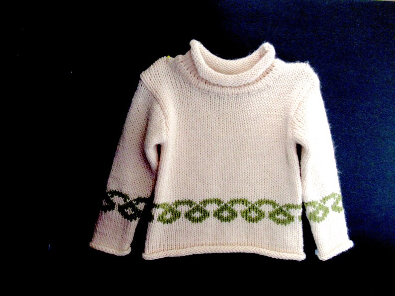 Pu&ograve; includere: Un maglione di lana bianco con un bordo verde intorno al collo e all'orlo inferiore. Il maglione ha un collo alto.