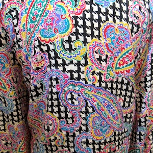 Pu&ograve; includere: Un capo colorato con un audace motivo paisley nei toni del rosa, blu, giallo e verde, su uno sfondo a pied de poule bianco e nero. Il tessuto ha un aspetto strutturato.