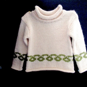 Pu&ograve; includere: Un maglione di lana bianco con un motivo a nodo celtico verde intorno al fondo e alle maniche.