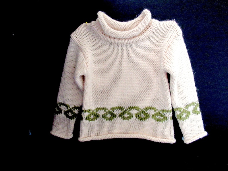 Pu&ograve; includere: Un maglione di lana bianco con un motivo a nodo celtico verde intorno al fondo e alle maniche.