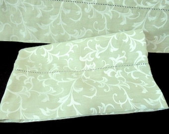 May include: A pair of light green bed pillowcases with a white floral pattern. The pillowcases have a subtle sheen and a delicate, embroidered edge.