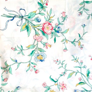 May include: A white fabric with a repeating pattern of green leaves and pink, blue, and yellow flowers.