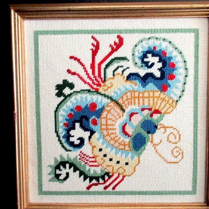 May include: A framed cross-stitch embroidery depicting a colorful, stylized dragon with blue, red, yellow, and green accents.