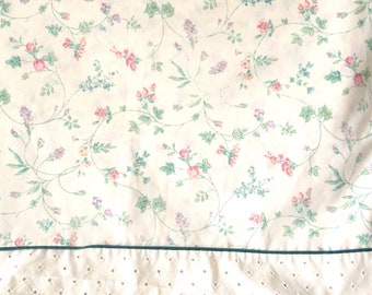 May include: White fabric with a delicate floral pattern in shades of pink, blue, and green. The fabric has a scalloped edge with a dark green trim.