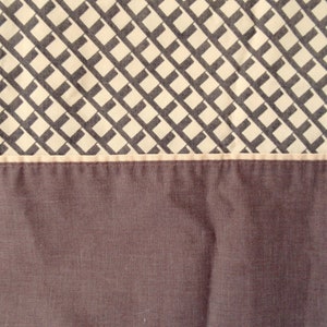 May include: A close-up of a brown fabric with a white and gray geometric pattern. The fabric has a seam along the top edge.