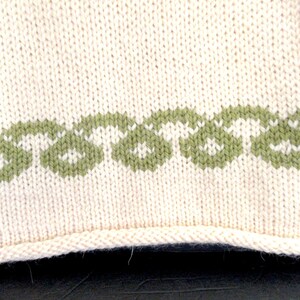 Pu&ograve; includere: Un primo piano di un tessuto a maglia con sfondo bianco e bordo verde. Il bordo &egrave; un motivo ripetitivo di piccole forme verdi.
