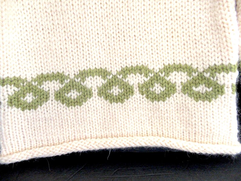 Pu&ograve; includere: Un primo piano di un tessuto a maglia con sfondo bianco e bordo verde. Il bordo &egrave; un motivo ripetitivo di piccole forme verdi.