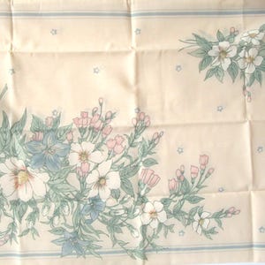 May include: Cream-colored fabric with floral patterns. The design features bouquets of white, pink, and blue flowers with green leaves. A light blue border and small star accents complete the design.
