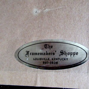 May include: A silver oval-shaped label with black text that reads "The Framemakers' Shoppe, Louisville, Kentucky, 897-3526".