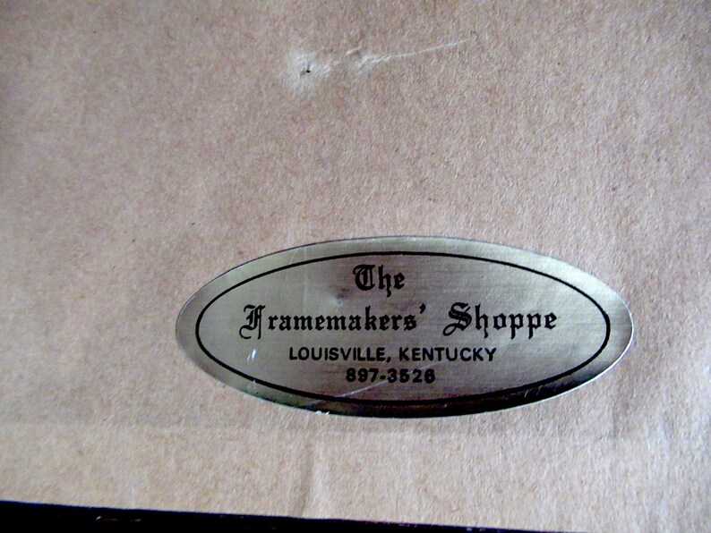May include: A silver oval-shaped label with black text that reads "The Framemakers' Shoppe, Louisville, Kentucky, 897-3526".