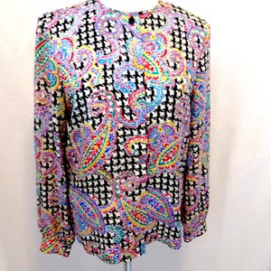 Pu&ograve; includere: Una camicetta a maniche lunghe con un vivace motivo paisley nei toni del rosso, giallo, blu e verde, su uno sfondo a pied-de-poule bianco e nero. La camicetta ha uno scollo tondo e una chiusura con un solo bottone.