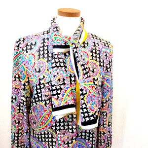 Pu&ograve; includere: Giacca con stampa paisley colorata e motivo a pied de poule, con sciarpa abbinata. Il design della giacca include tonalit&agrave; vivaci di rosso, blu, giallo e verde. La sciarpa ha strisce bianche e nere con un centro giallo.