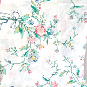 May include: White fabric with a floral pattern. The flowers are pink, blue, and yellow. The leaves are green.
