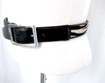 May include: A black leather belt with a silver buckle and a zebra print design.