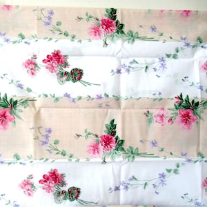 May include: A rectangular fabric panel featuring alternating horizontal bands of solid white and light beige. The fabric is decorated with a repeating floral pattern of pink geraniums, green leaves, and small purple flowers arranged in clusters.