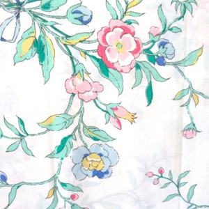 May include: A white fabric with a floral pattern featuring pink, blue, and yellow flowers with green leaves.