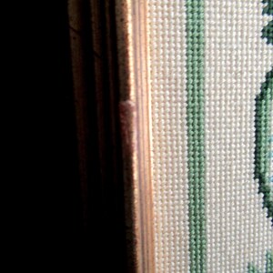 May include: Close-up of a framed needlepoint piece with a floral design. The design features blue, green, and red flowers on a white background.
