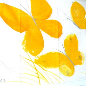 May include: A white fabric featuring three yellow butterflies with painted brushstroke textures. The design includes thin gray lines for butterfly bodies and antennae, yellow grass blades at the bottom, and the signature "Vana" with a small yellow bug icon.