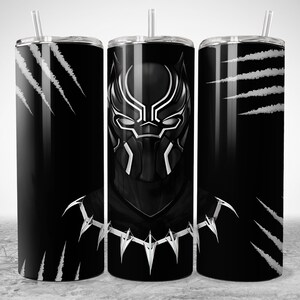 Puede incluir: Vaso con tem&aacute;tica de Pantera Negra con pajita. El dise&ntilde;o presenta la m&aacute;scara de Pantera Negra y marcas de garras sobre un fondo negro. El vaso es cil&iacute;ndrico y tiene una tapa plateada.