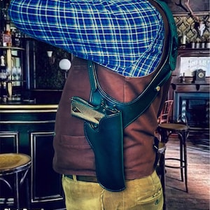 May include: A brown leather shoulder holster with a black gun inside. The holster is worn over a brown vest and a blue plaid shirt.