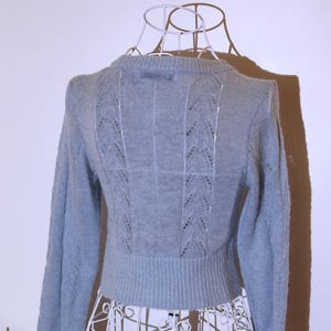 Puede incluir: Un su&eacute;ter azul claro con mangas largas y cuello redondo. La parte trasera del su&eacute;ter presenta un dise&ntilde;o calado decorativo con patrones verticales y diagonales. El su&eacute;ter se exhibe en un maniqu&iacute; de alambre blanco.