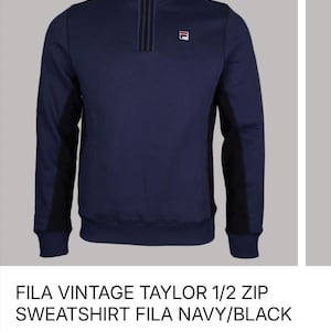 May include: Navy blue Fila Vintage Taylor 1/2 zip sweatshirt. The sweatshirt features a black panel on the sides and a zipper closure. The Fila logo is visible on the chest. The text "FILA VINTAGE TAYLOR 1/2 ZIP SWEATSHIRT FILA NAVY/BLACK" is displayed.