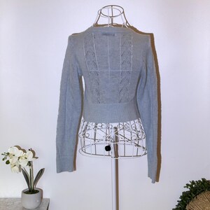 Puede incluir: Un su&eacute;ter azul claro con mangas largas y cuello redondo. La parte trasera del su&eacute;ter presenta un dise&ntilde;o de punto calado decorativo. El su&eacute;ter se exhibe en un maniqu&iacute; de alambre blanco.