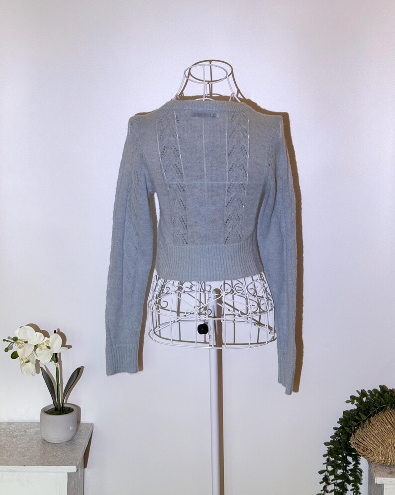 Puede incluir: Un su&eacute;ter azul claro con mangas largas y cuello redondo. La parte trasera del su&eacute;ter presenta un dise&ntilde;o de punto calado decorativo. El su&eacute;ter se exhibe en un maniqu&iacute; de alambre blanco.