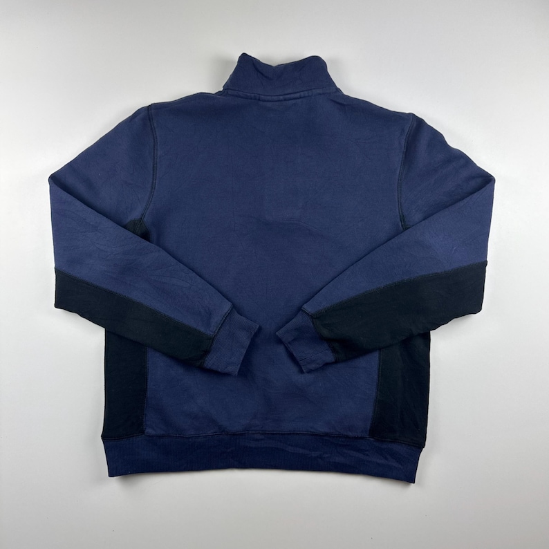 May include: Navy blue sweatshirt with a high collar and black panels on the sleeves. The sweatshirt is made of a soft material and has a relaxed fit. The garment is laid flat on a light gray surface.