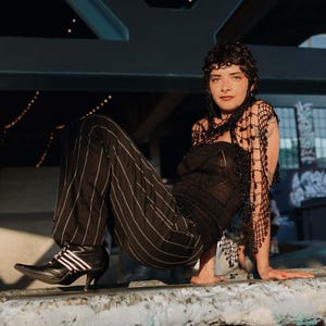 May include: A black strapless knit top, black pinstriped trousers, and a black beaded crochet shawl. The outfit is paired with black pointed-toe ankle boots featuring white side stripes and a mid-height heel, creating a cohesive dark ensemble.