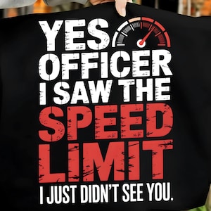May include: Black t-shirt with the text "YES OFFICER I SAW THE SPEED LIMIT I JUST DIDN'T SEE YOU." The text is in white and red, with a speedometer graphic at the top. The shirt is held up by a person.
