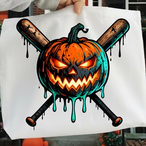 May include: White tote bag featuring a Halloween-themed graphic. The design includes a menacing orange pumpkin with glowing eyes and a jagged mouth, crossed baseball bats, and dripping accents. The artwork has a cartoonish style.