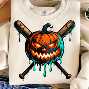 May include: Cream-colored sweatshirt featuring a Halloween-themed graphic. The design includes a menacing orange pumpkin with glowing eyes and a jagged mouth, crossed with two wooden baseball bats. Black drips accent the design.