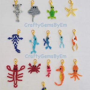 May include: A collection of fourteen beaded charms shaped like various sea creatures, including a hammerhead shark, stingray, turtle, starfish, whale, fish, crab, lobster, seahorse, and octopus, each attached to a small gold-tone lobster clasp.