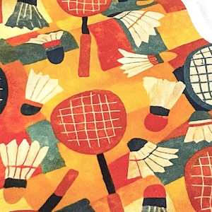 May include: A colorful pattern featuring badminton rackets and shuttlecocks in shades of red, orange, yellow, and blue. The design has a geometric, artistic style, with the sports equipment arranged in a repeating pattern.