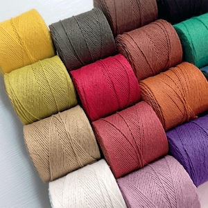 Könnte beinhalten: Eine Sammlung farbenfroher Garnrollen in verschiedenen Farbtönen, darunter Gelb, Grün, Rot und Braun. Das Garn ist eng gewickelt und erzeugt eine strukturierte Oberfläche. Das Bild zeigt eine Vielzahl von Farben, perfekt für Bastel- und DIY-Projekte.