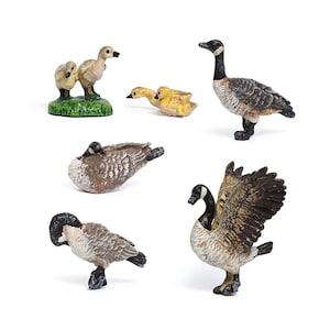 Pode incluir: Uma coleção de figuras de gansos em miniatura. O conjunto inclui gansos adultos com cabeças e pescoços pretos e corpos castanhos e brancos, juntamente com vários gansinhos amarelos. Alguns gansos estão em pé, enquanto outros estão em várias poses.