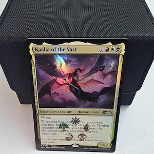 Peut inclure: Une carte à collectionner Magic: The Gathering holographique intitulée Kaalia of the Vast, représentant une figure ailée avec une épée. La carte affiche le texte Legendary Creature - Human Cleric, la capacité de vol et des règles de jeu.