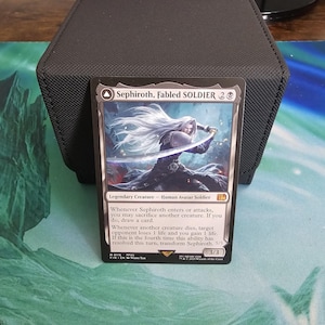 May include: A collectible trading card featuring Sephiroth, Fabled Soldier. The card depicts a character with long white hair wielding a sword. The card has a black border and includes game text. The card is a 3/3.