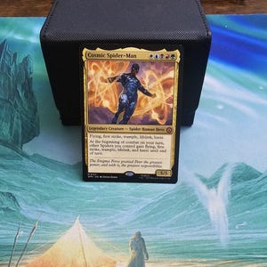 May include: A Cosmic Spider-Man Magic: The Gathering trading card featuring a dark blue suited hero surrounded by golden energy swirls. The card text includes the name, mana symbols, creature type, abilities, and a 5/5 power and toughness rating.