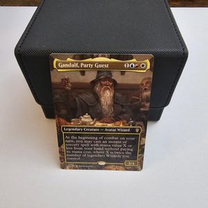 Op de afbeelding: Een Magic: The Gathering ruilkaart getiteld Gandalf, Party Guest, met een illustratie van een bebaarde tovenaar met een hoed aan een tafel met eten en drinken. De kaart toont de tekst Legendary Creature - Avatar Wizard en spelregels.