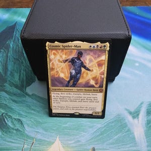 May include: A Cosmic Spider-Man Magic: The Gathering trading card featuring a dark-suited figure surrounded by golden energy swirls. The card text includes the name, mana symbols, creature type, abilities, and flavor text in English.