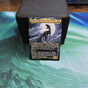 Könnte beinhalten: Eine Magic: The Gathering Sammelkarte mit dem Titel Indoraptor, the Perfect Hybrid. Die Karte zeigt eine Dinosaurier-Illustration vor einem Vollmond, mit schwarzen Textfeldern, die Fähigkeiten sowie Stärke und Widerstandskraft von 3/1 beschreiben.