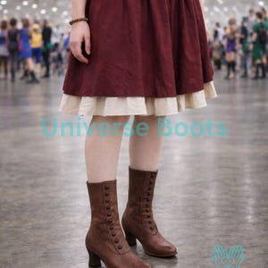 Puede incluir: Botines de cuero marrón con cierres de botones y tacones pequeños. Las botas se usan con una falda burdeos y una enagua color crema. La imagen también incluye el texto "Universe Boots" y "HANDMADE WITH LOVE".