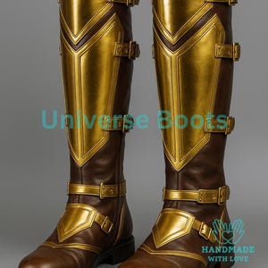 May include: A pair of knee-high brown boots with gold-colored accents and buckles. The boots feature a geometric design on the front and sides, with the text "Universe Boots" and "HANDMADE WITH LOVE" visible.