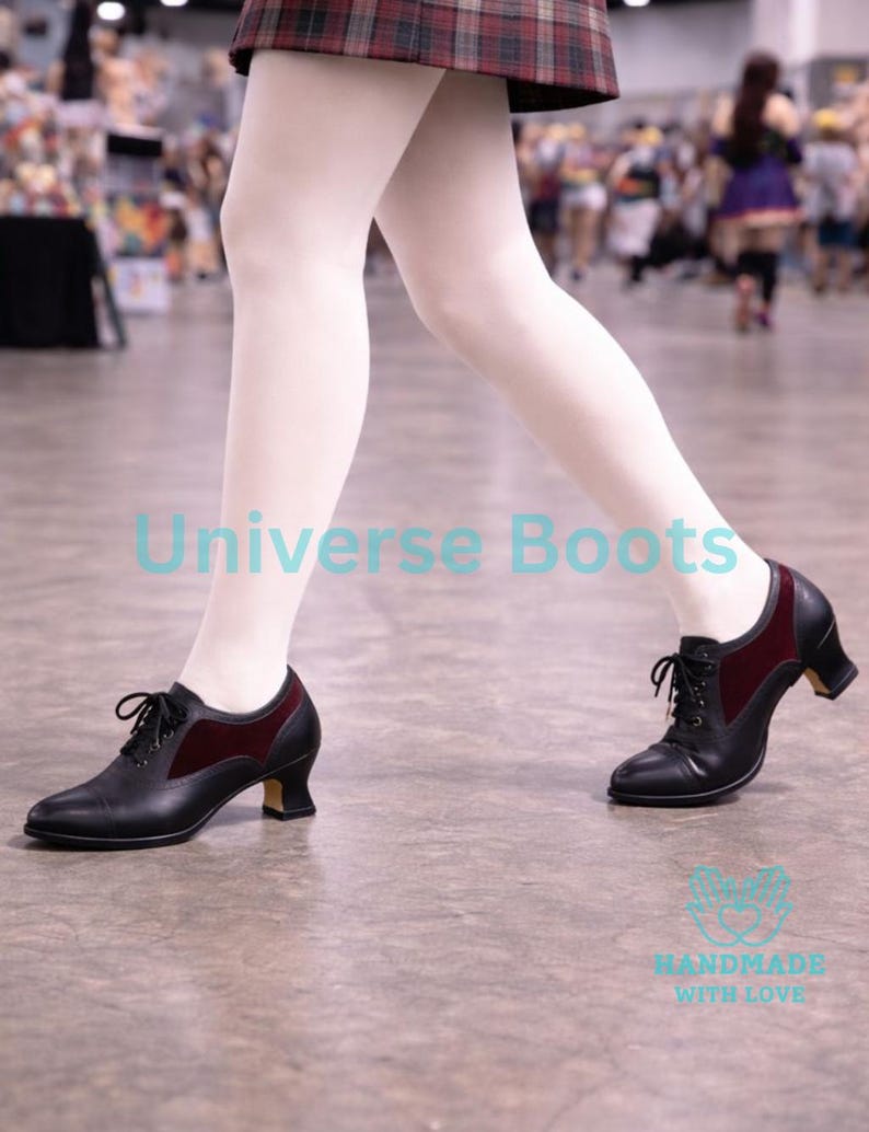 May include: Black leather lace-up shoes with a burgundy velvet accent on the sides. The shoes have a small heel and are worn with white tights. The text "Universe Boots" and "Handmade with Love" are visible.