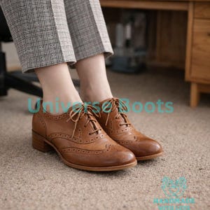 May include: Brown leather Oxford shoes with decorative perforations and laces. The shoes have a low heel and are worn with gray plaid pants. The shoes are on a beige carpet.