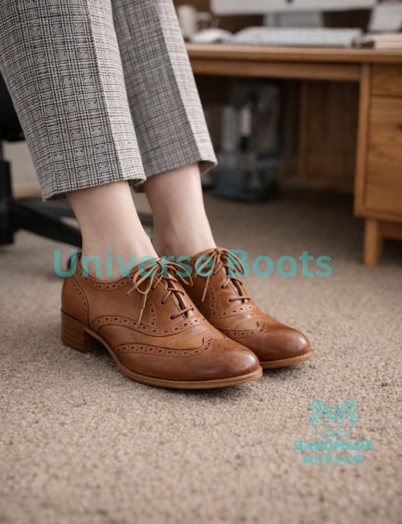 May include: Brown leather Oxford shoes with decorative perforations and laces. The shoes have a low heel and are worn with gray plaid pants. The shoes are on a beige carpet.