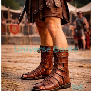Op de afbeelding: Bruine leren gladiatorsandalen met meerdere bandjes en metalen studs. De sandalen hebben een veterontwerp en worden gedragen met een bruine leren rok. De afbeelding is buiten gemaakt.