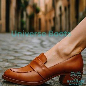 May include: Tan leather loafers with a block heel. The shoes feature a classic design with a strap across the top. The image also includes the text "Universe Boots" and "HANDMADE WITH LOVE".